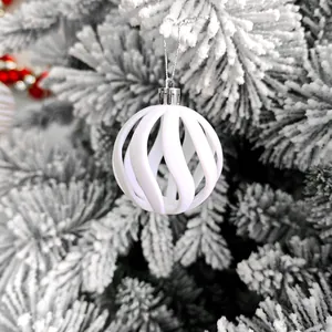 Détail d'une boule de Noël blanche de 6cm ajourée en spirale suspendue à un sapin enneigé
