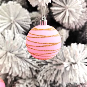 Boule de Noël rose avec rayures dorées pailletées sur un sapin de Noël blanc