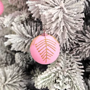 Gros plan d'une boule de Noël rose avec motifs dorés sur des branches de pin enneigées