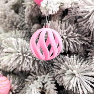 Boule de Noël en velours rose avec spirale ajourée suspendue à une branche enneigée
