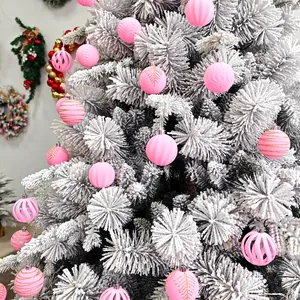 Gros plan de boules de Noël roses floquées avec des motifs pailletés sur un sapin enneigé