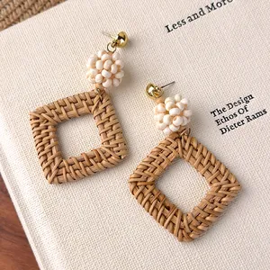 Nahaufnahme von gewebten Boho-Rattan-Ohrringen mit weißen Perlen auf einem Buch