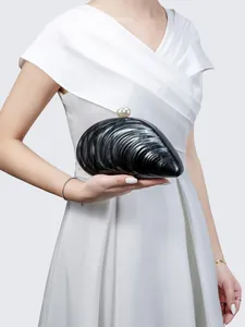 Detail der muschelförmigen Abendtasche mit schwarzer Wellentextur und Perlenverschluss am Model