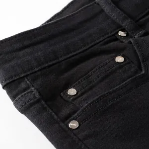 Detail of slim fit black jeans featuring silver metal rivets and high-quality denim texture