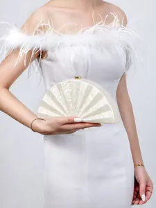 Detail of a pearl white acrylic fan-shaped clutch with a gold buckle for wedding attire