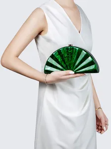 Detail of green acrylic fan clutch bag with marble texture held by a model in white dress