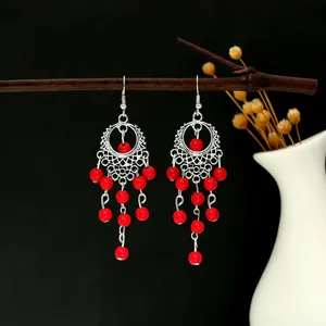 Détail de boucles d'oreilles bohèmes argentées avec glands en perles rouges et turquoise