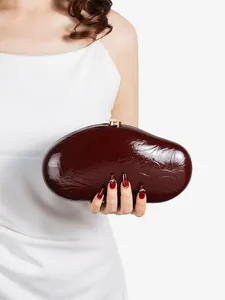 Detail of burgundy glossy patent leather clutch bag with elegant gold spherical clasp