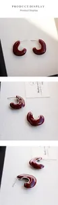 Macro detail of burgundy C-shaped hoop earrings with high-gloss enamel and silver studs