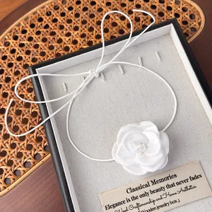 Détail du collier choker camélia en tissu blanc avec un long ruban sur plateau à bijoux