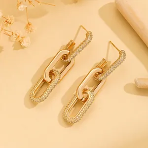 Elegant gold chain earrings with sparkling zircons on a warm minimalist background