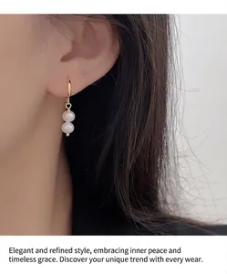 Détail de deux perles blanches suspendues à un anneau d'oreille doré minimaliste