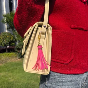 Detail of bright pink tassel charm with gold clip on a cream PU leather shoulder bag