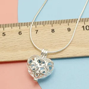Macro view of a 2.5cm hollow heart-shaped pearl cage locket pendant on a sleek snake chain