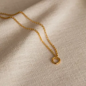 Close-up of minimalist gold geometric circle necklace on textured beige fabric