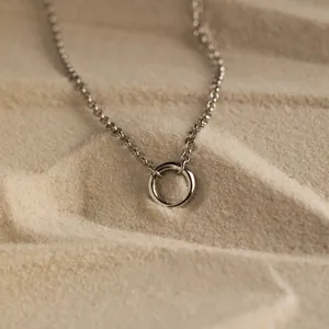Minimalist geometric circle pendant necklace in silver finish on a textured sand background