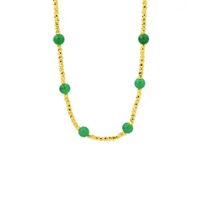 Minimalist gold beaded necklace featuring vibrant emerald green accent beads on white background