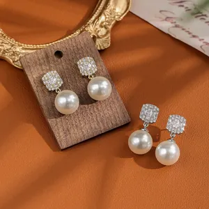 Detail of elegant pearl drop earrings with rectangular zircon studs in gold and silver