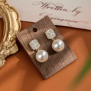 Detail of luxury pearl drop earrings with zircon square studs on vintage wood display