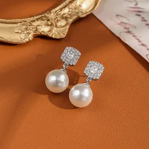Detailed view of elegant pearl drop earrings with sparkling crystals on orange leather