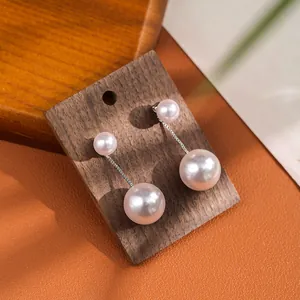 Close-up of double pearl drop earrings with elegant silver chains on a dark wood background