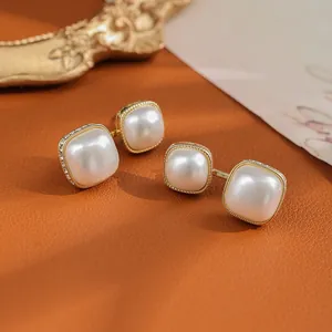 Detail of vintage square pearl earrings with gold twisted edge on a leather background