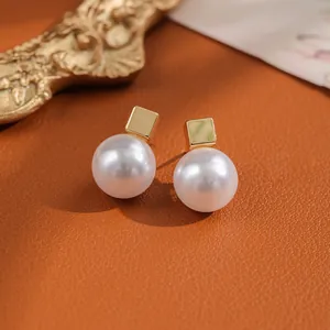 Macro shot of minimalist pearl earrings with gold-plated squares on textured leather surface