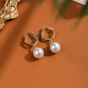Detail of gold pearl earrings with zircon square studs on premium brown leather backdrop