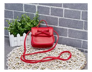 Detail of red mini crossbody bag with bow decoration and white stitching on a straw mat