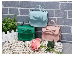 Detailed view of mini girls' bow handbags in blue, green, and pink on straw mat