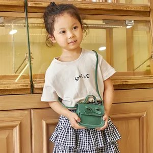 Mini green girls' shoulder bag with bow and white stitching shown on young model
