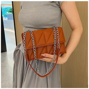 Detail of caramel quilted shoulder bag with chunky silver chain worn by a model
