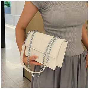 Detail of white quilted crossbody bag with silver chain strap shown on model shoulder