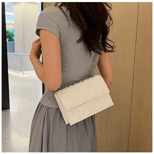 Detail view of cream quilted chain bag worn by a model in a modern interior setting
