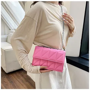 Detail of a bright pink quilted crossbody bag with silver chain strap on model