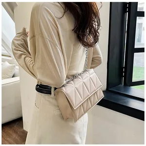 Detail of a beige quilted leather chain bag worn as a shoulder bag by a model