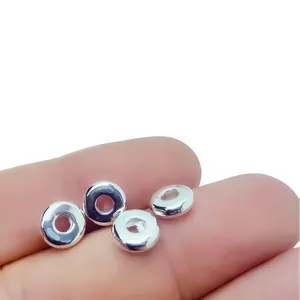 Macro detail of polished silver spacer beads shown on a fingertip for size reference