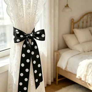 Black polka dot satin bow tie curtain tieback shown on white lace drapes in a bedroom