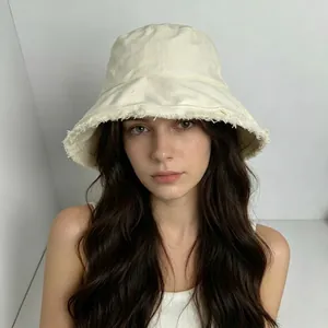 Off-white canvas bucket hat with frayed edges worn by a model against a plain wall