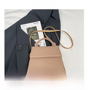 Close-up of khaki crossbody bag with knot handle next to a smartphone for size reference