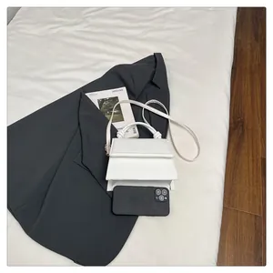Mini white crossbody bag with knot handle next to a smartphone for size comparison