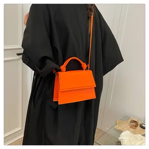 Detail of a bright orange crossbody bag featuring a unique knotted handle design