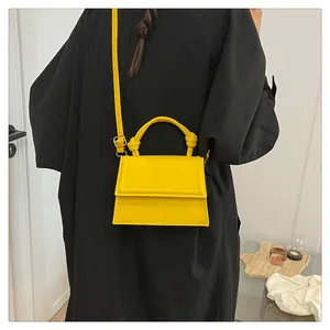 Detail of a bright yellow small square crossbody bag featuring a stylish top handle knot