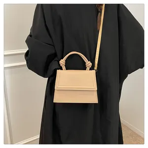 Detail of elegant beige crossbody bag featuring a unique knotted handle and slim strap