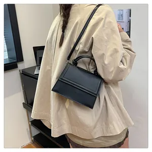 Minimalist black matte leather crossbody bag shown on a model in an indoor lifestyle setting