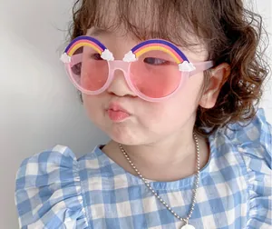 Pink translucent children's sunglasses with rainbow and cloud charms worn by model