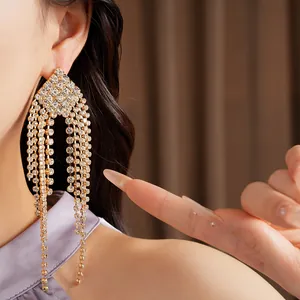 Detailed macro view of sparkling gold-tone rhinestone tassel earrings on model
