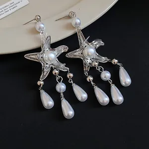 Detail view of silver starfish earrings with teardrop pearls and tassels