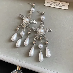 Macro view of starfish earrings featuring elegant water drop pearl tassels on gray velvet tray