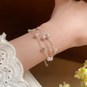 Detailansicht eines mehrlagigen Silberarmbands mit rosa Perlen am weiblichen Handgelenk